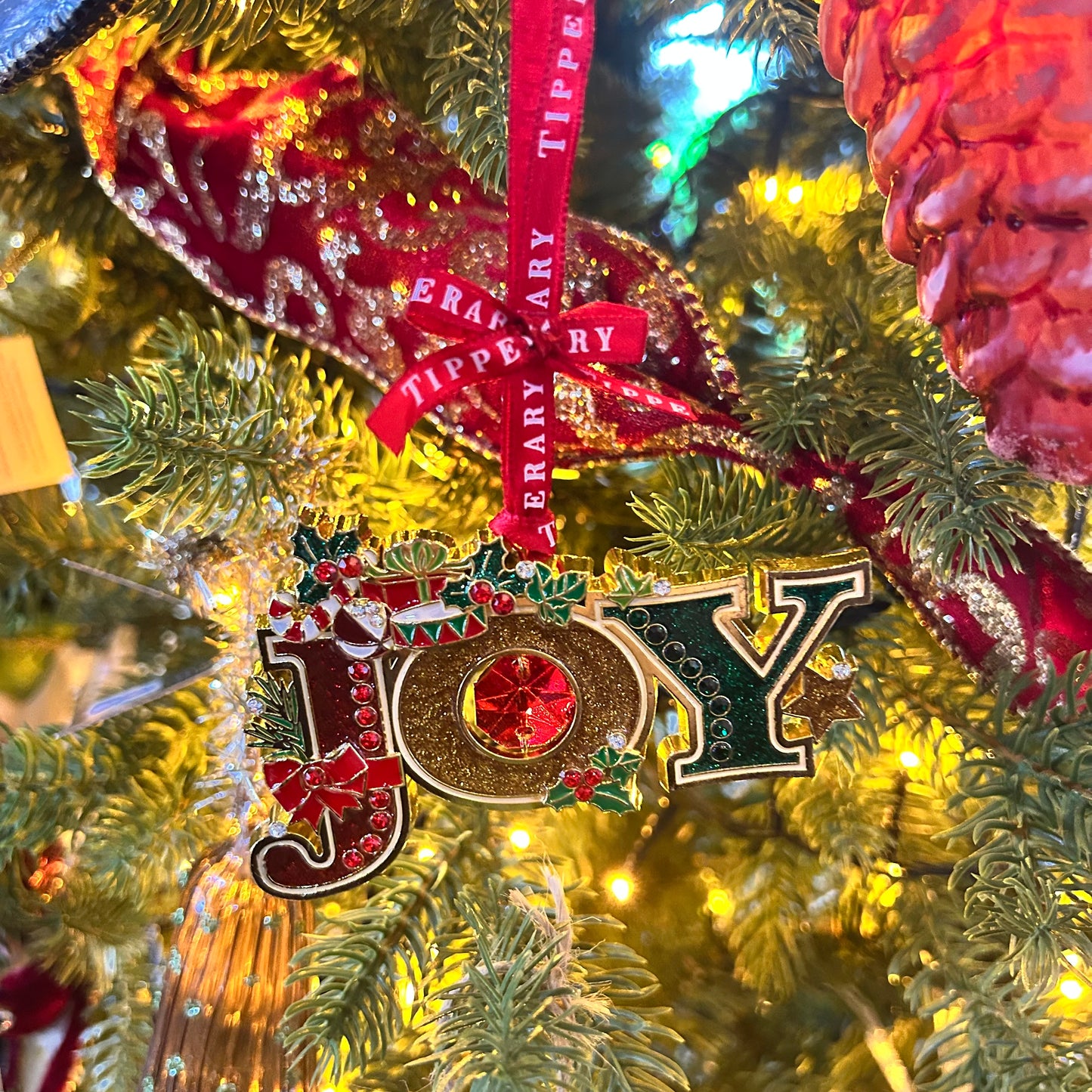 Decorative ornament spelling 'JOY' on a Christmas tree with red ribbon.