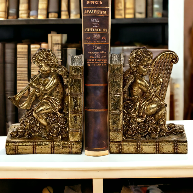 Two vintage gold cherub bookends with one bookend showing an angel playing a musical instrument and the other bookend showing an angel holding a harp. Both bookends are placed on a white surface with a background of books.