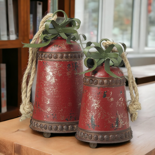 Two vintage style red metal hanging bells with green jute ropes, placed on a wooden surface.