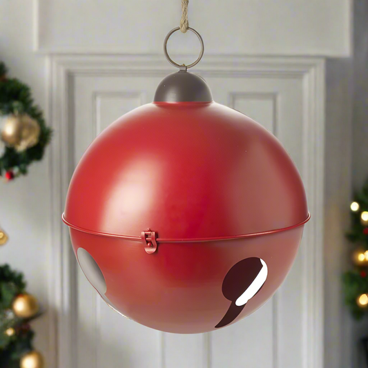 A large red metal bell with a metallic finish, hanging by a jute rope, displayed in a home setting with Christmas decorations around.