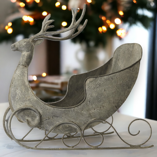 A vintage style zinc reindeer sleigh decoration with a rustic finish, displayed in a home setting during the Christmas season.