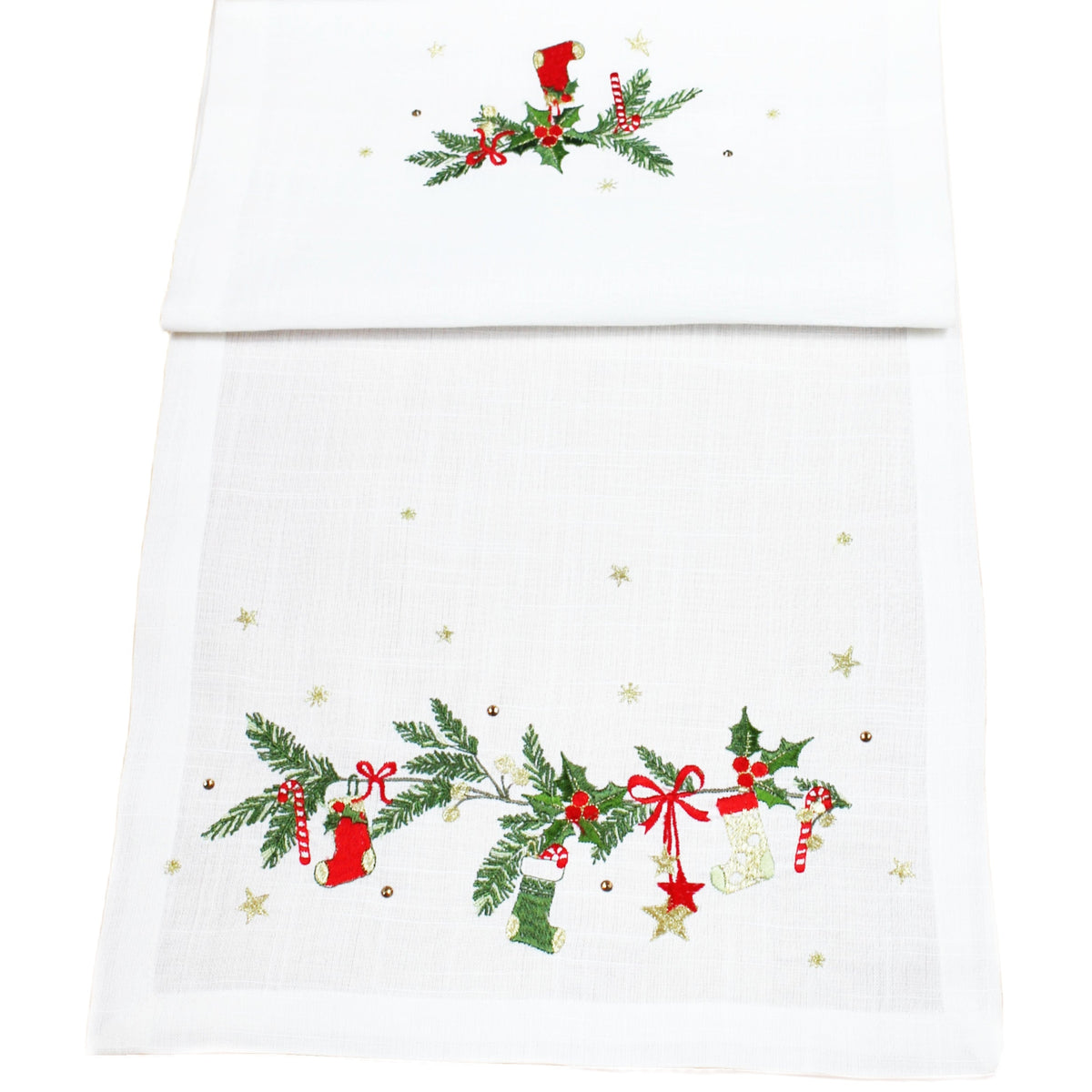 A white table runner with embroidered Christmas garlands, including green holly and pine branches, red bows, red stockings, and small gold stars.