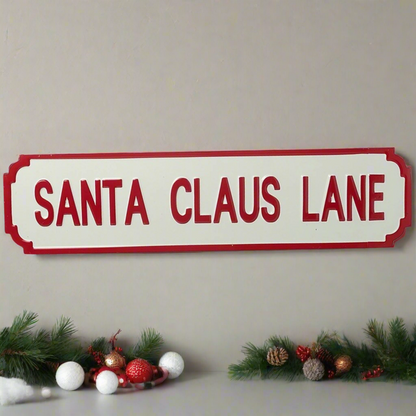 A Santa Claus Lane sign with a red background and white text, surrounded by Christmas decorations including pine branches and festive ornaments.