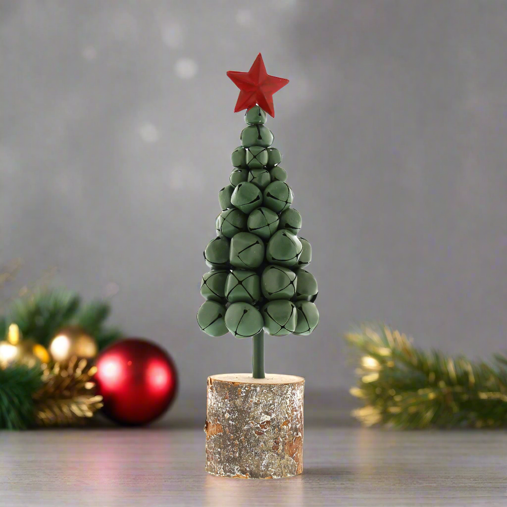 A green Christmas bells tree with a red star on top, arranged on a rustic wooden log base.