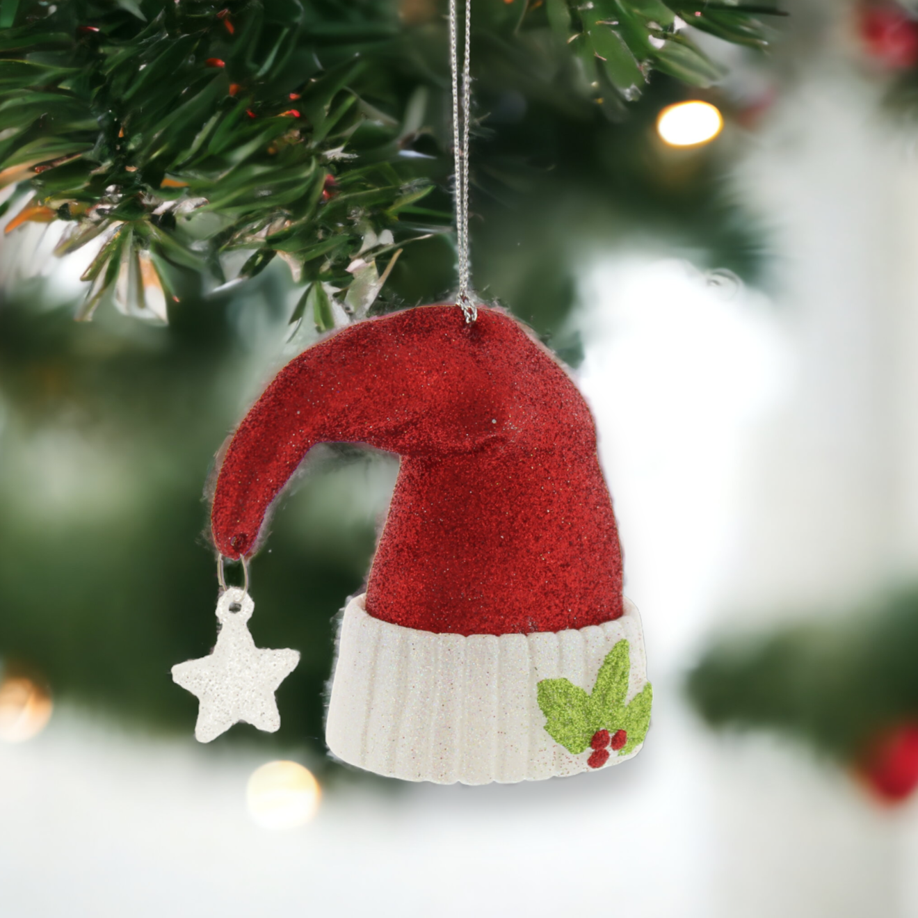 A red glitter Santa hat with a star hanging from the top and foliage on the rim, displayed on a Christmas tree.