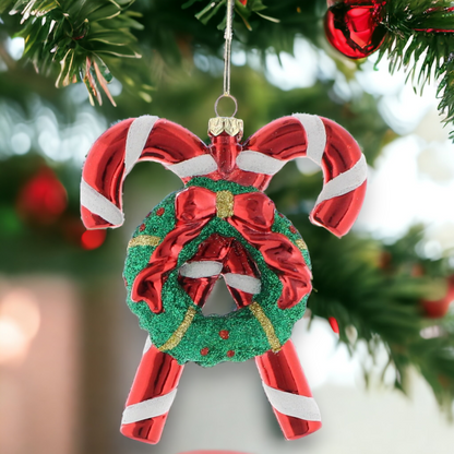 A red and white striped candy cane with a green wreath and a bow, hanging from a Christmas tree.