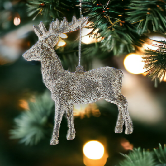 A silver reindeer hanging decoration displayed on a Christmas tree with lights in the background.