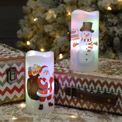 Two lit Christmas LED Pillar candles with Santa and snowman designs, displayed on vintage patterned suitcases in front of a softly blurred Christmas tree.