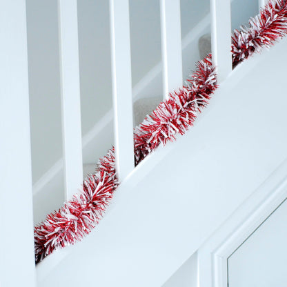 A strand of chunky red and white Christmas tinsel hanging on a white staircase.
