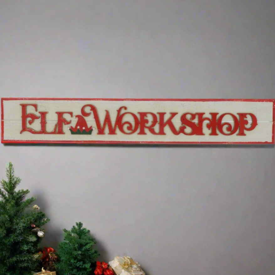 A wooden sign with 'ELF WORKSHOP' written in red and white, placed against a neutral background with a Christmas tree and decorations in the peripheral.