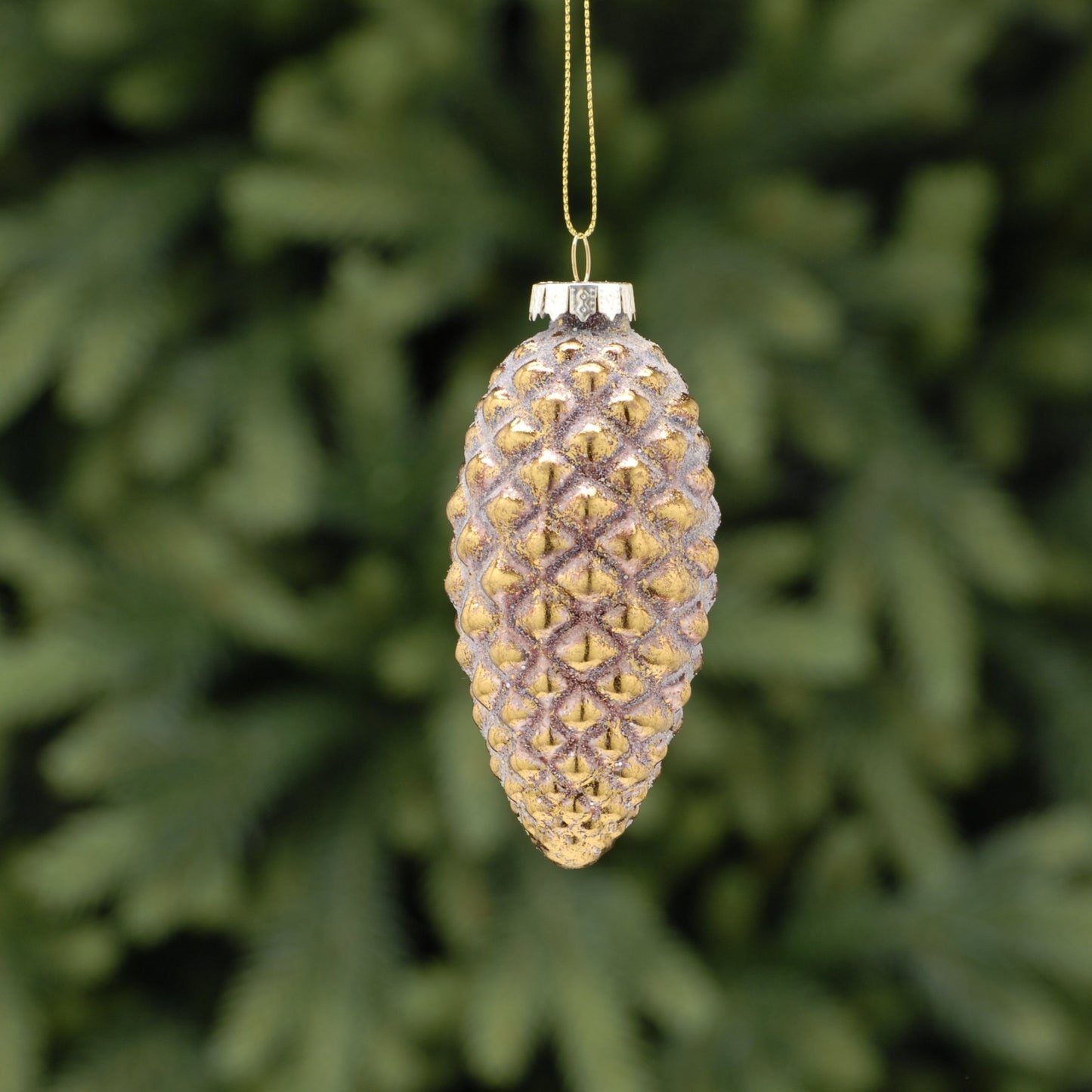 A pink and antique gold effect pinecone-shaped Christmas decoration hanging from a wire against a green foliage background.