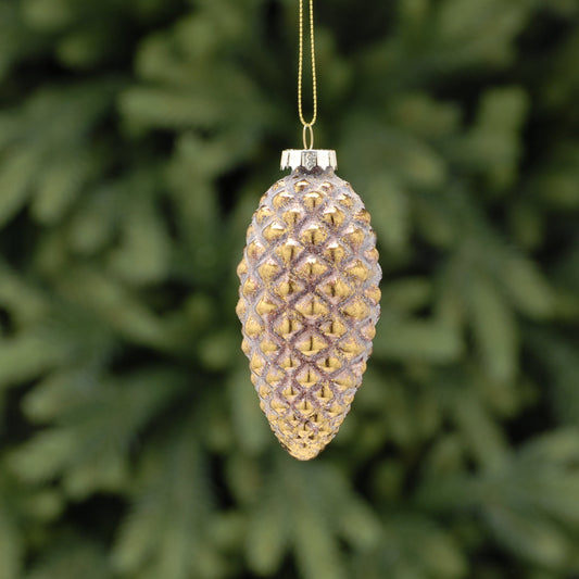 A pink and antique gold effect pinecone-shaped Christmas decoration hanging from a wire against a green foliage background.