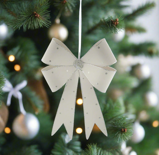 A white metal bow with silver glitter Christmas decoration, displayed on a Christmas tree with lights and decorations.