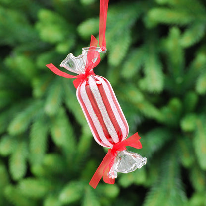 A hanging glass decoration shaped like a candy cane with a red ribbon, set against a blurred green background.