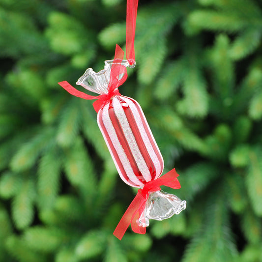 A hanging glass decoration shaped like a candy cane with a red ribbon, set against a blurred green background.