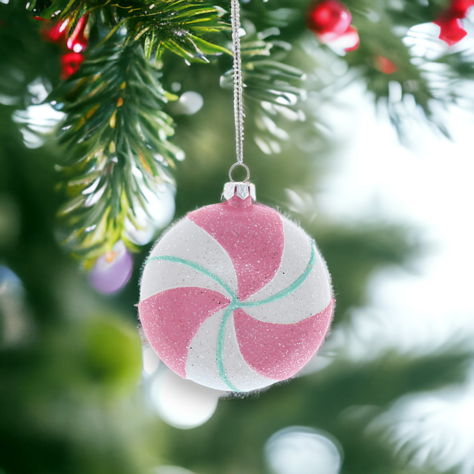 A pink, green, and white round sweet hanging Christmas decoration with glitter, placed on a Christmas tree.