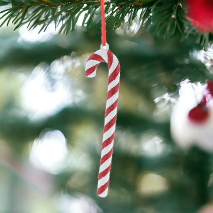 A hanging decoration featuring a red and white striped candy cane with glitter, attached to a red hanging string on a Christmas tree.
