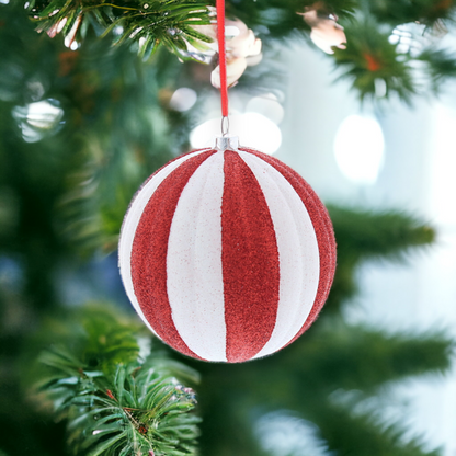 A red and white striped glittery candy cane ball hanging from a tree.