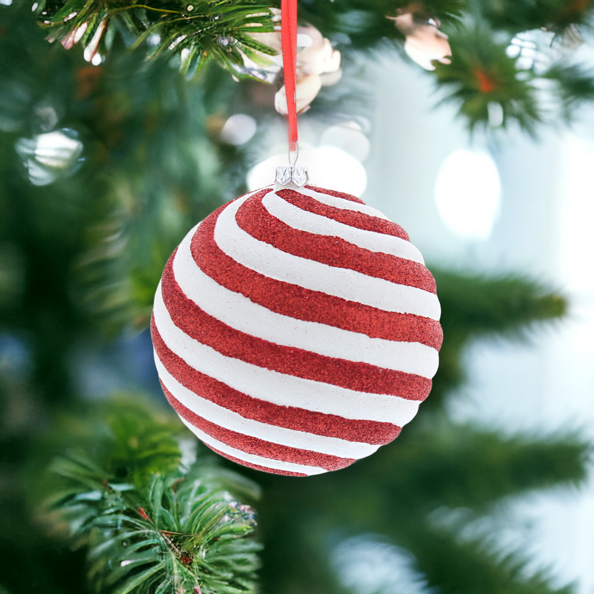 A red and white striped candy cane-shaped hanging decoration with glitter, placed on a Christmas tree.