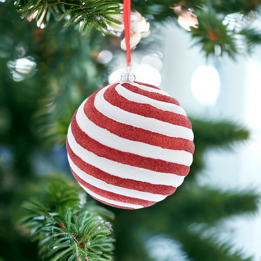 A red and white striped candy cane-shaped hanging decoration with glitter, placed on a Christmas tree.