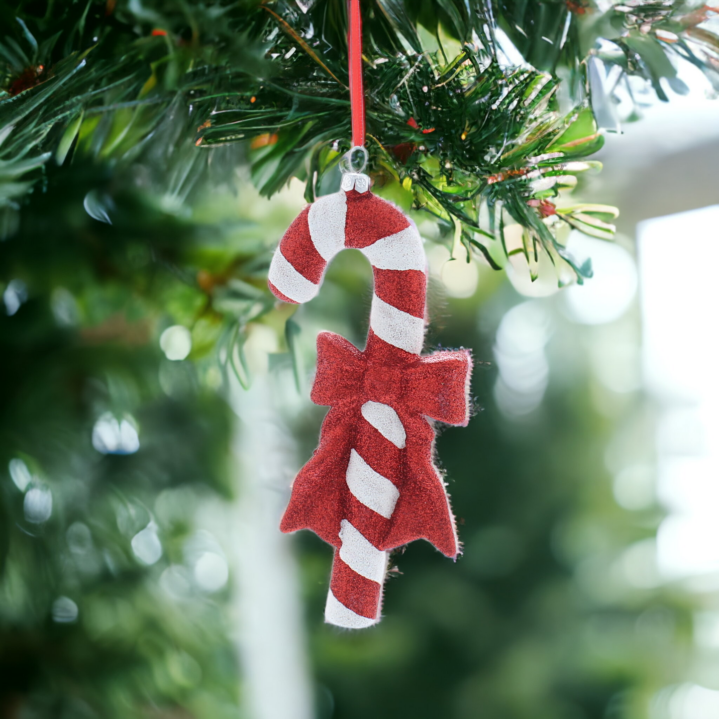 A glittery red and white candy cane Christmas ornament with a bow hanging from a string.