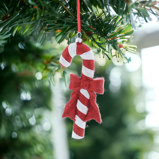 A glittery red and white candy cane Christmas ornament with a bow hanging from a string.