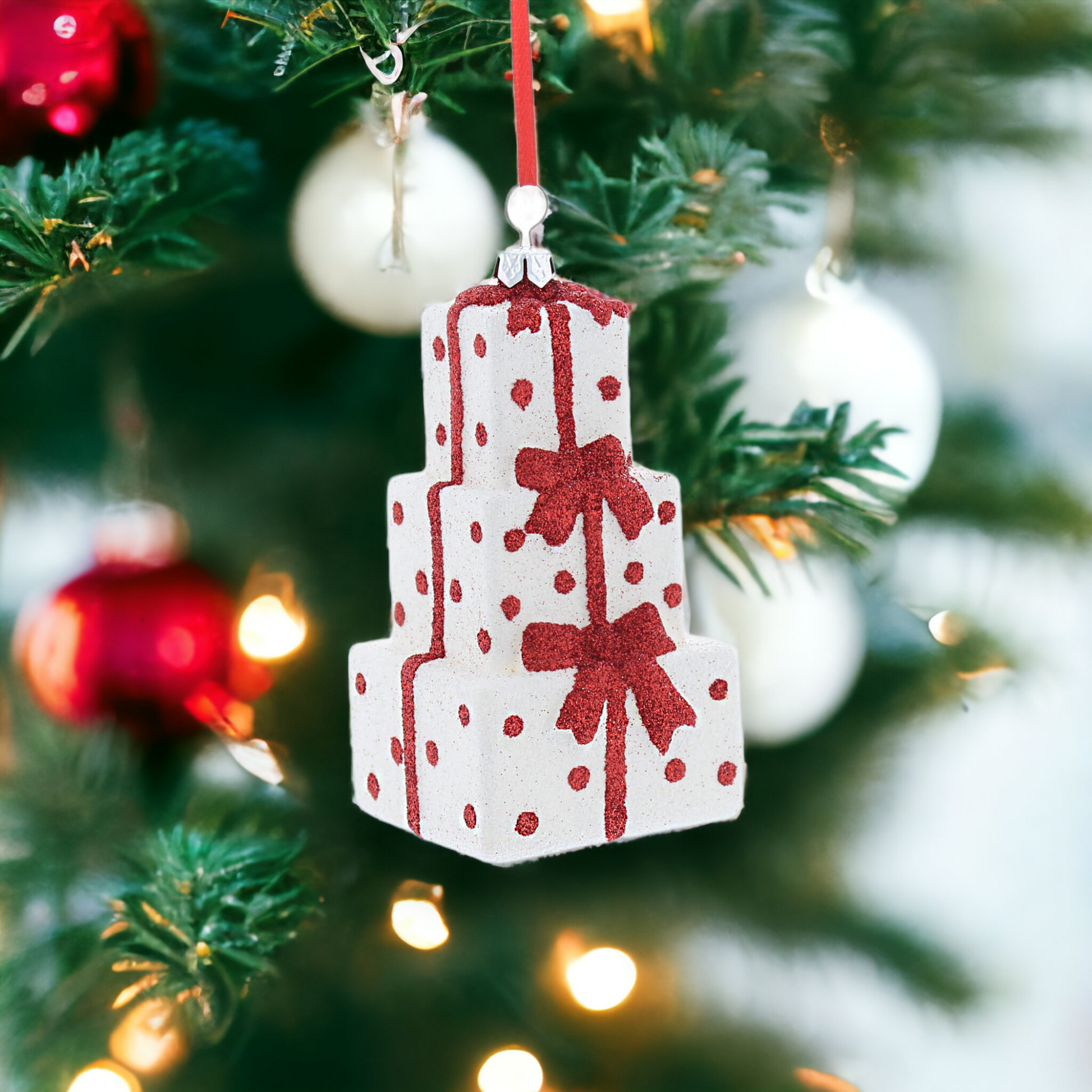 A glittery red and white stacked presents hanging decoration with a red hanging string, placed on a Christmas tree.