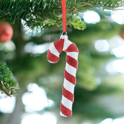 A red and white glittery candy cane hanging from a tree with Christmas balls and green needles in the background.