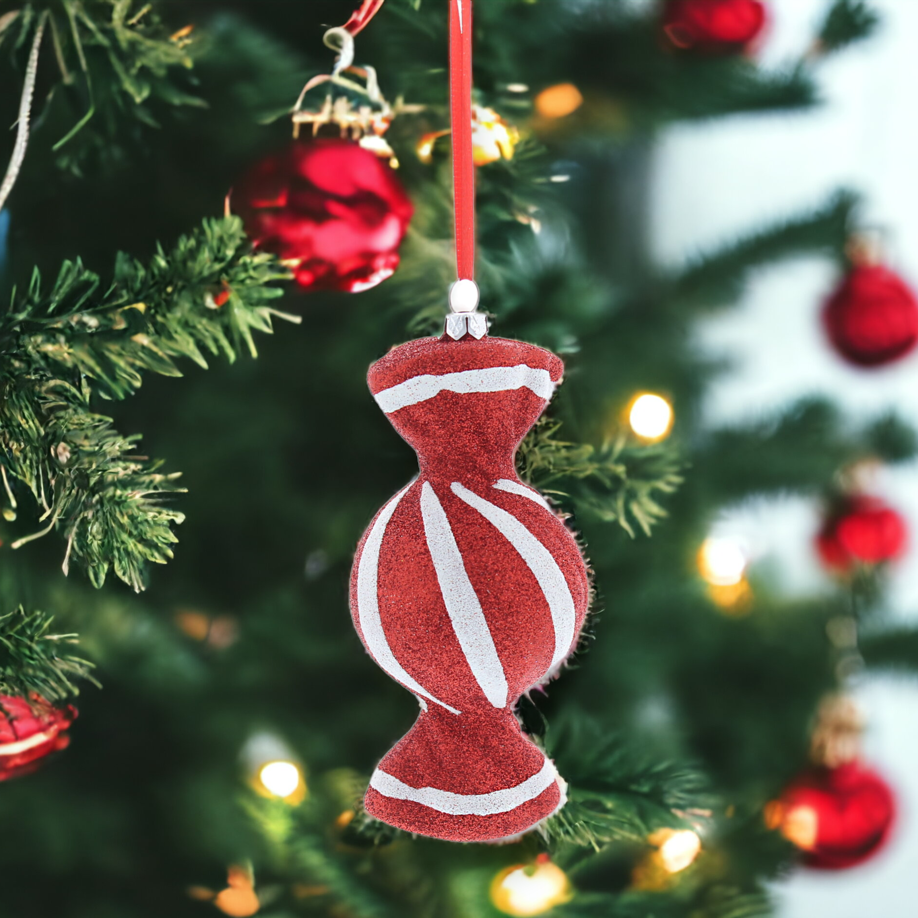A red and white striped hanging decoration resembling a Christmas ornament, with a glittery finish, displayed on a Christmas tree.