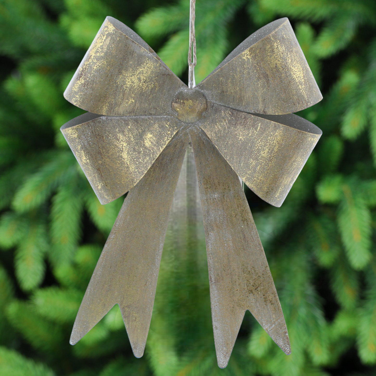 A decorative aged gold metal bow with a vintage distressed finish, designed as a Christmas tree ornament, displayed against a blurred green background.