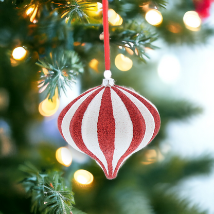 A red and white glittery teardrop-shaped hanging decoration on a Christmas tree with holiday lights.