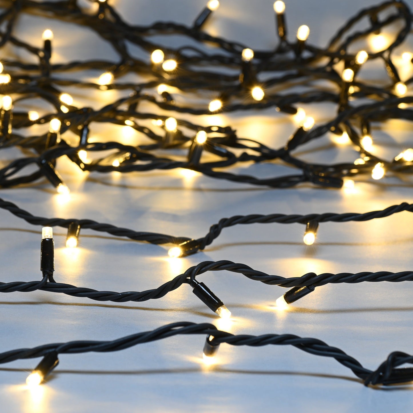 A close-up of Festive Christmas fairy lights with warm white LED bulbs on a black cable.