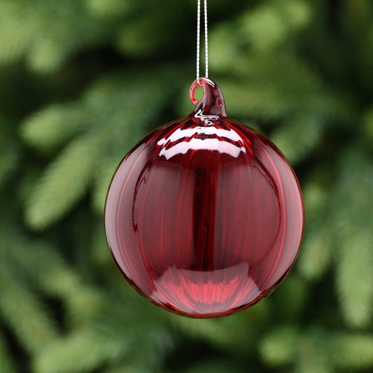 A translucent red glass Christmas tree bauble with a silver hanging wire, displayed against a green foliage background.