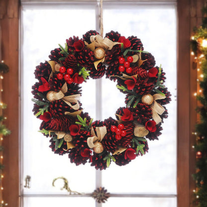 A Red Rose and Pinecone Christmas Wreath displayed indoors, featuring green foliage, red wooden flowers, berries, and golden baubles.
