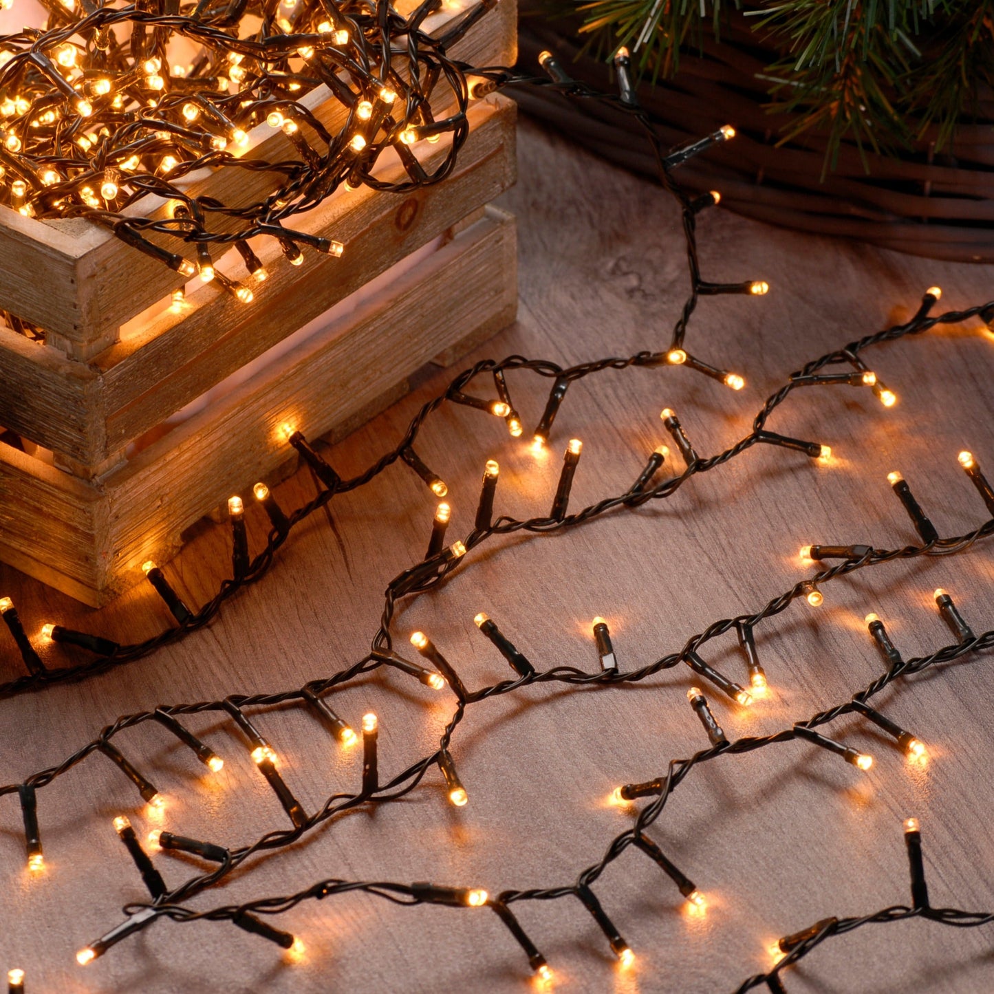 String of warm white Christmas lights placed on a wooden surface with a blurred Christmas tree in the background.