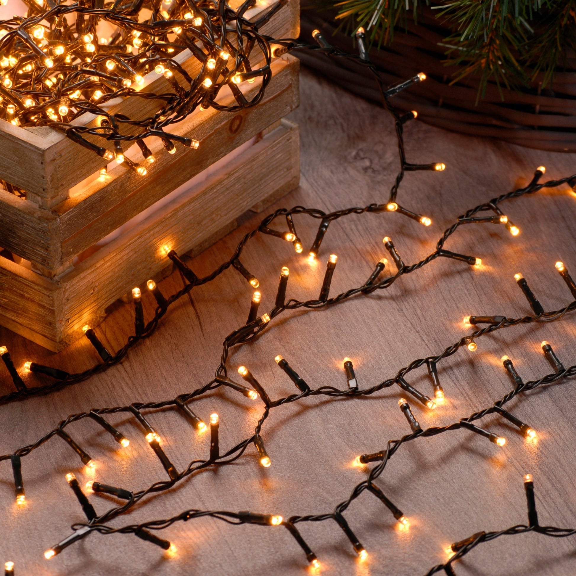 String of warm white Christmas lights placed on a wooden surface with a blurred Christmas tree in the background.
