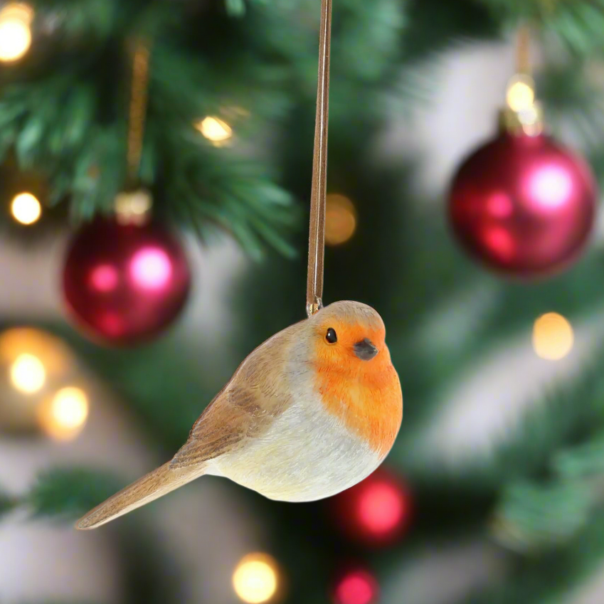 A brown and white robin hanging from a ribbon on a Christmas tree, with red and green ornaments and lights in the background.