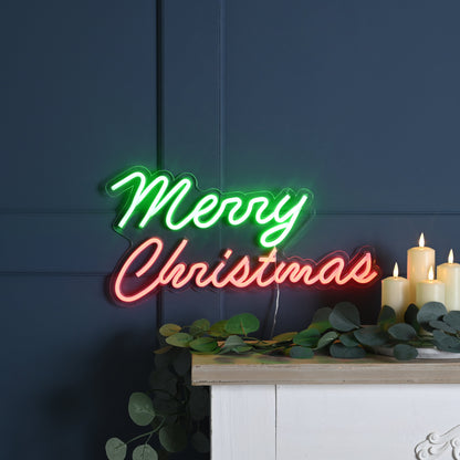Neon sign with 'Merry Christmas' on a dark blue wall with candles and greenery.