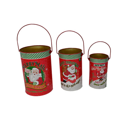 Three vintage-style Christmas metal buckets with red handles, decorated with Santa Claus illustrations and holiday text on a plain white background.