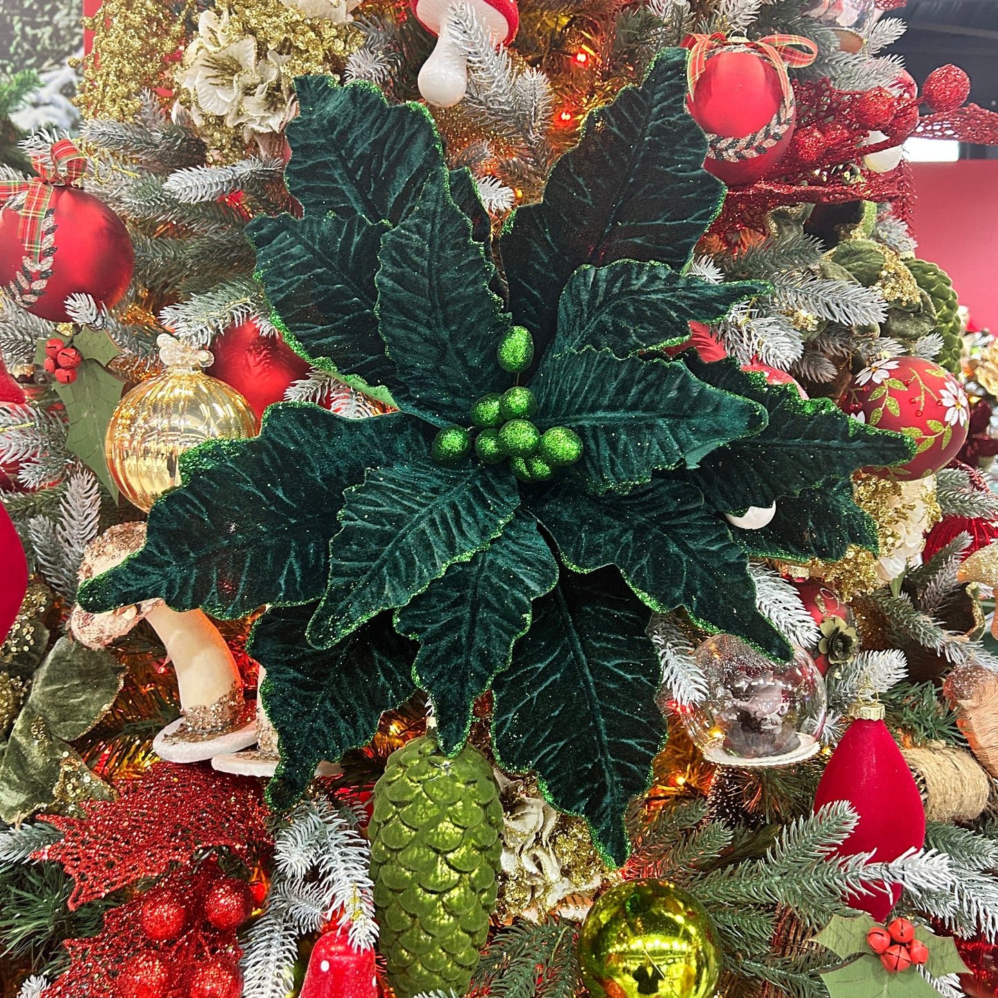 A dark green Christmas poinsettia stem with glitter, placed in a festive Christmas tree with red and gold decorations.