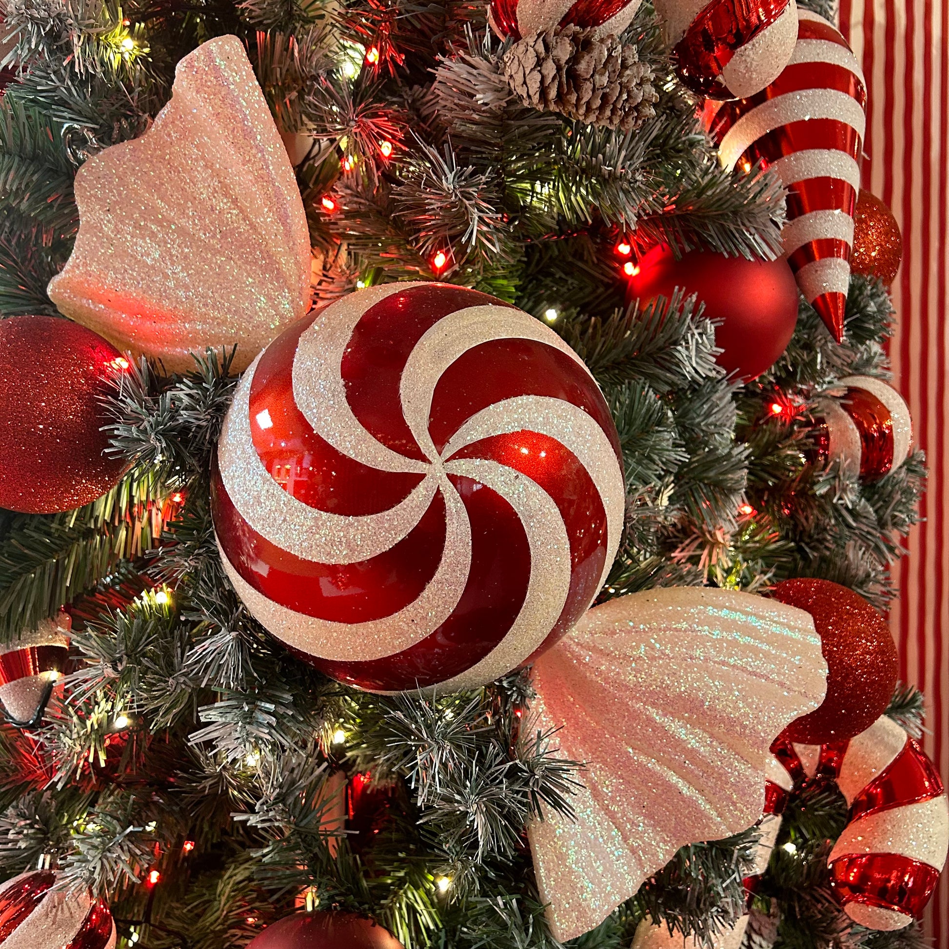 A decorative candy cane-shaped ornament on a Christmas tree, surrounded by red and white striped candy canes with white tips.