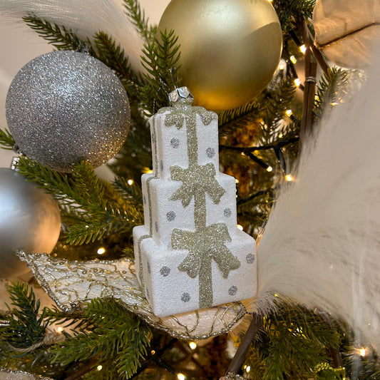 A white, gold, and silver stacked present hanging decoration with glitter, displayed on a Christmas tree.
