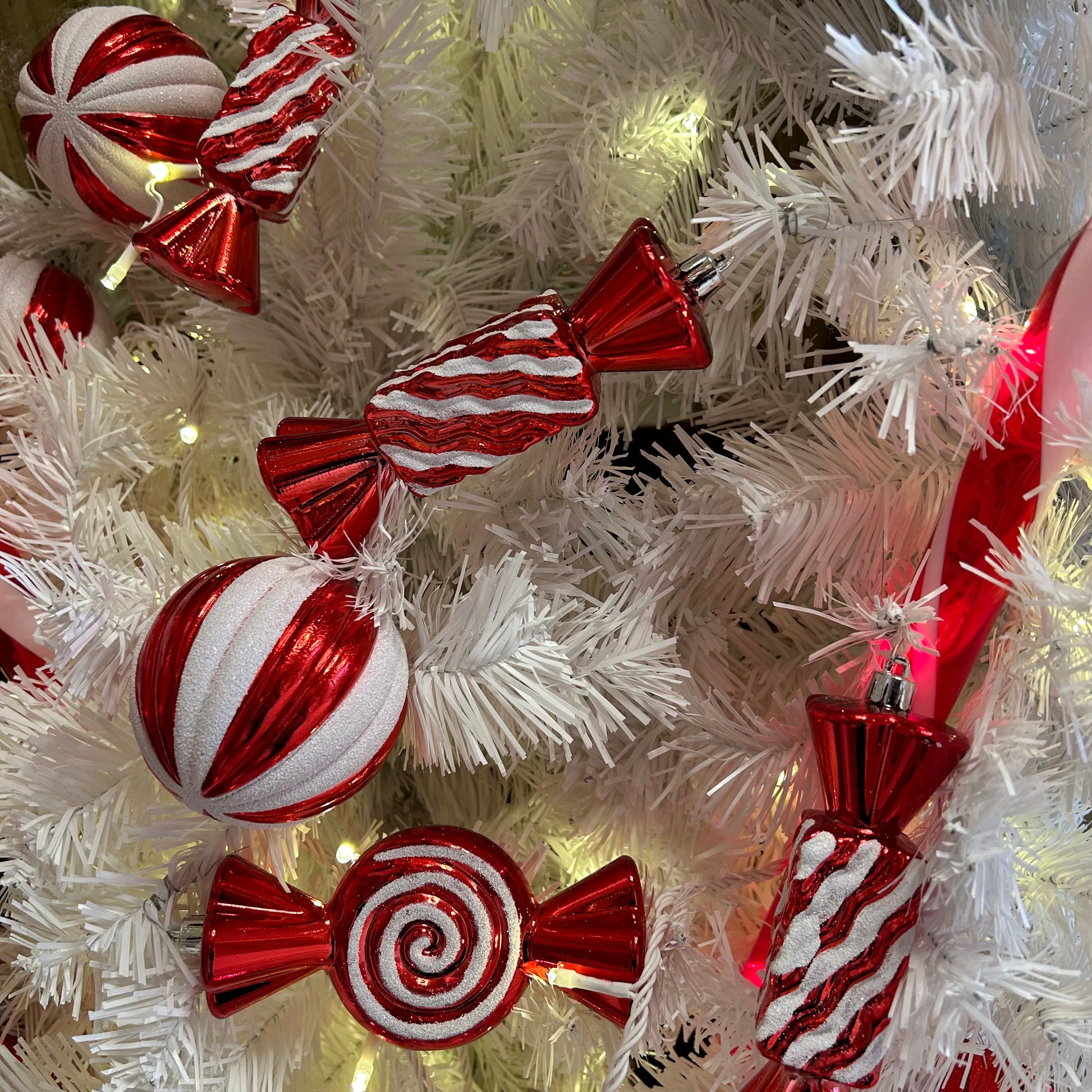 A set of striped candy cane Christmas baubles in red and white, displayed on a Christmas tree with lights.