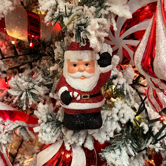 A red glittery Santa Claus ornament with gold hanging wire, displayed on a Christmas tree.