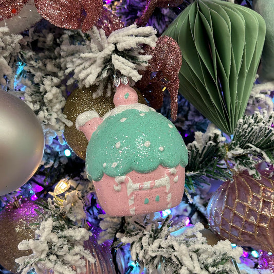 A pink, green, and white cupcake-shaped hanging decoration with glitter and a silver hanging wire, displayed on a Christmas tree.