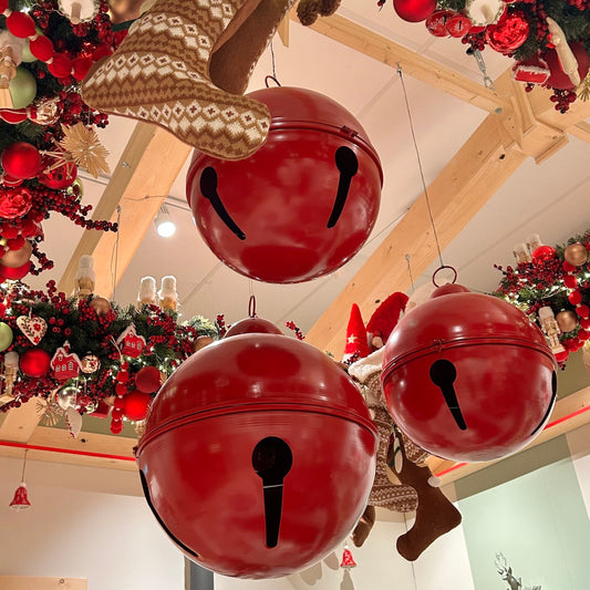 Set of three red oversized metal Christmas bell decorations hanging indoors, likely intended for festive holiday decor.