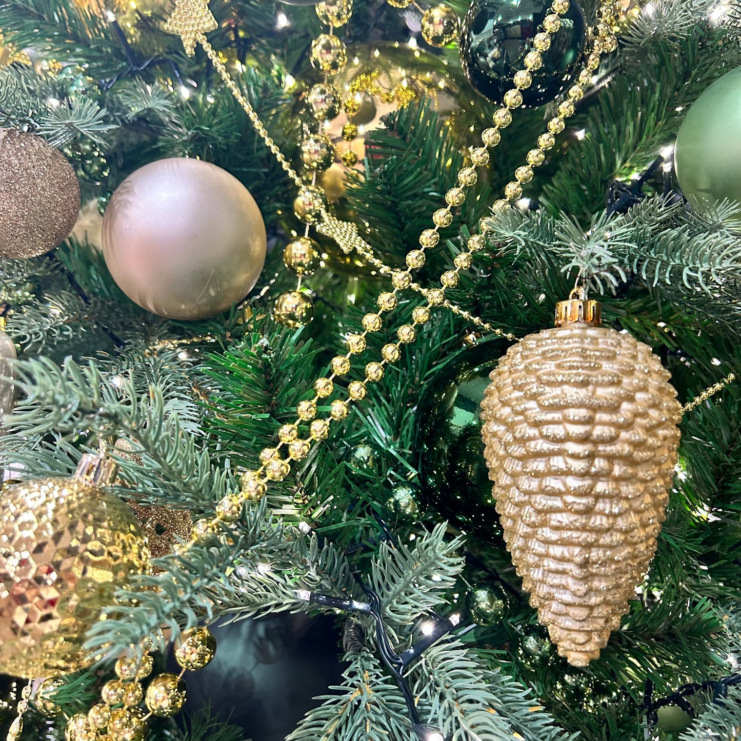 A close-up of a golden bead garland adorning a Christmas tree, showcasing its shiny beads and ornate tassel.