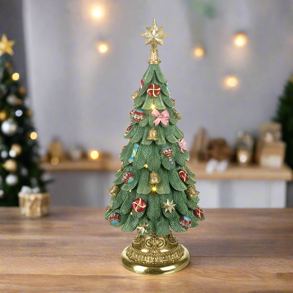 A Christmas tree ornament with a star on top, set on a wooden surface with a blurred Christmas tree in the background.