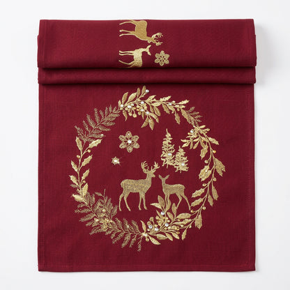 A deep burgundy fabric table runner with gold embroidered holiday motifs, including a wreath with deer, trees, and snowflakes, shown against a plain white background.