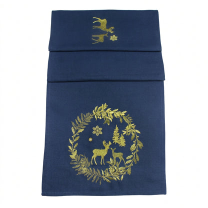 A navy blue table runner with gold embroidered holiday motifs, including a wreath with deer and snowflakes, shown against a white background.